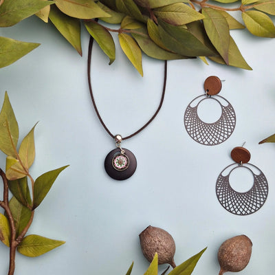 Jewelry set with earrings and necklace on a pale background surrounded by green leaves and matching earrings.