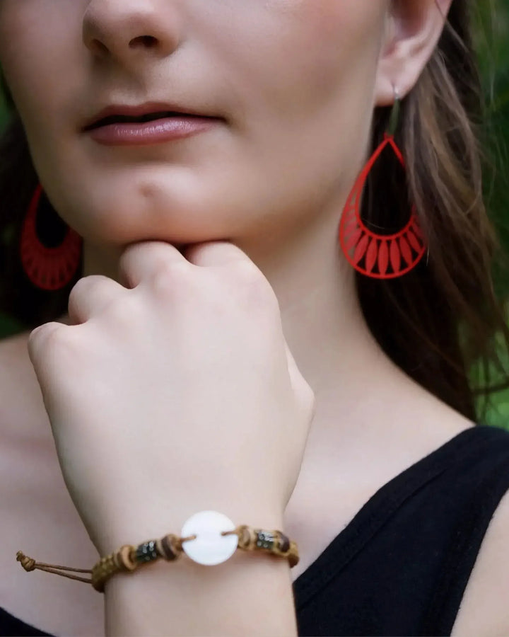 Model wearing bright orange Leafy Droplet Filigree Drop Earrings against green foliage