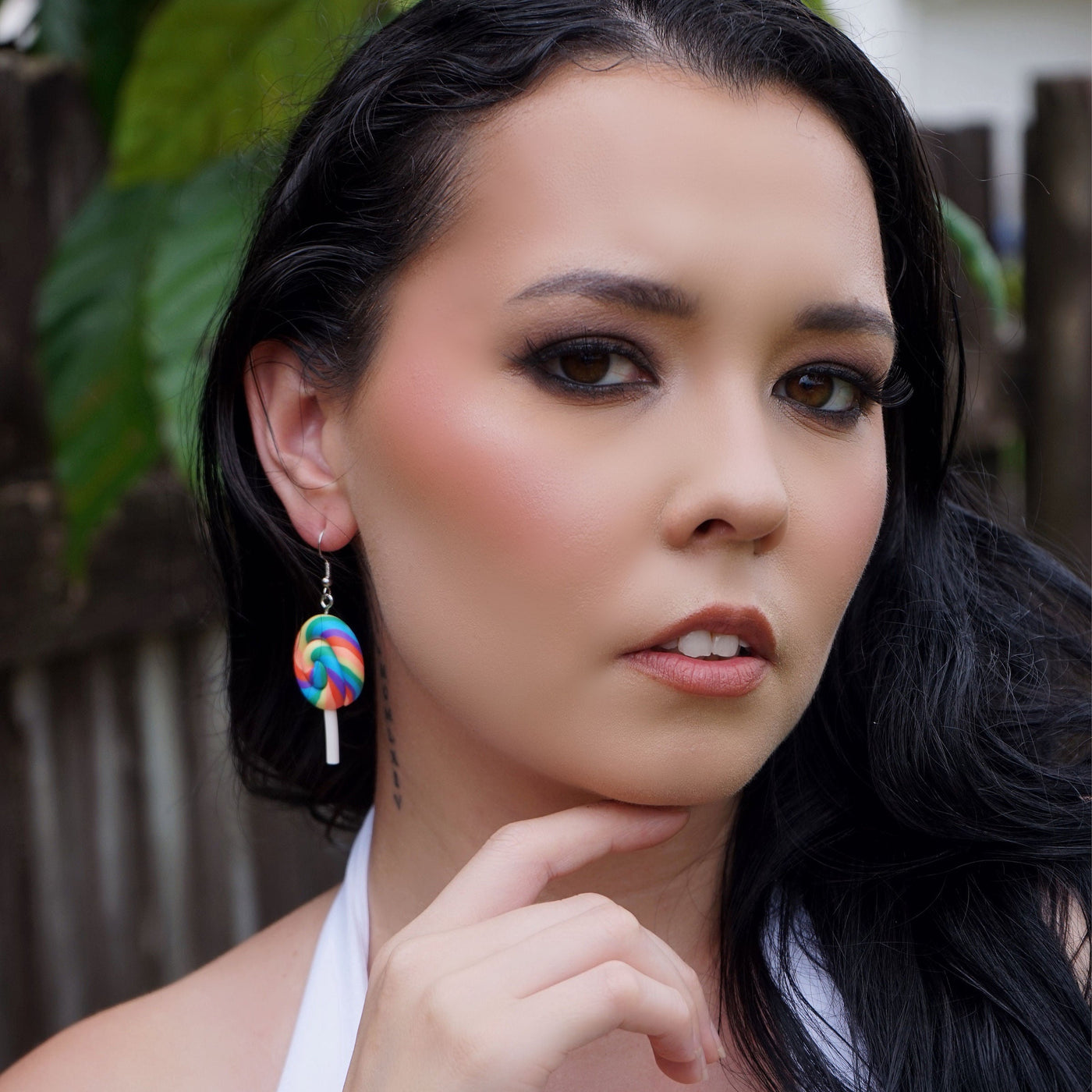 Woman wearing large novelty lollipop earrings in a backyard setting