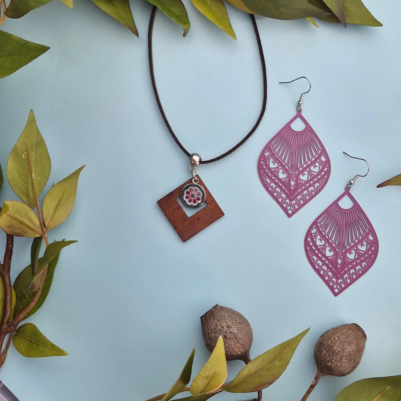 Earrings on a pale blue background with  with green leaves and pink earrings.