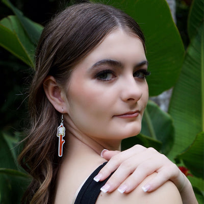 Woman wearing a marshmallow on a stick earring with a green leafy background