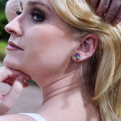 Side view of a woman with blonde hair and colorful mermaid glitter earrings, outdoors.