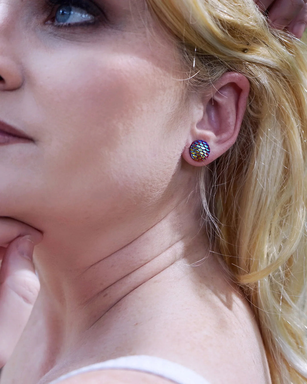 Close-up of a woman with blonde hair wearing mermaid glitter earrings, with a blurred background.