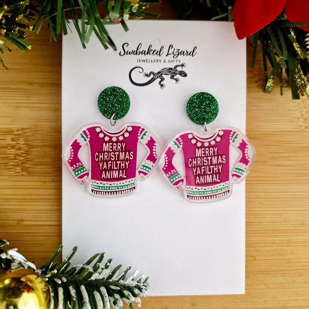 Earrings resembling Christmas sweaters on a branded card with festive decorations.