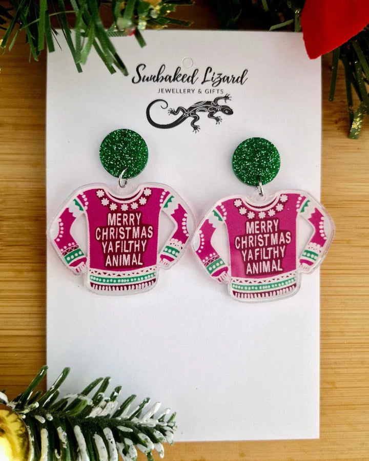Earrings resembling Christmas sweaters on a branded card with festive decorations.