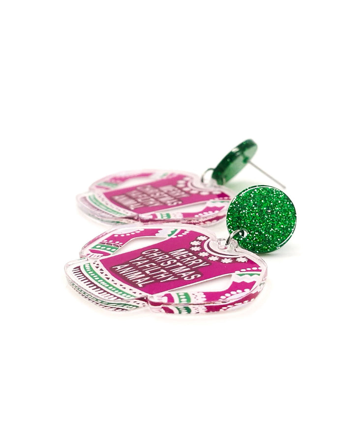Detail photo of earrings shaped like pink Christmas sweaters with text on a white background