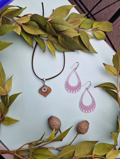 Pink earrings and mandala charm necklace on a pale background with green leaves