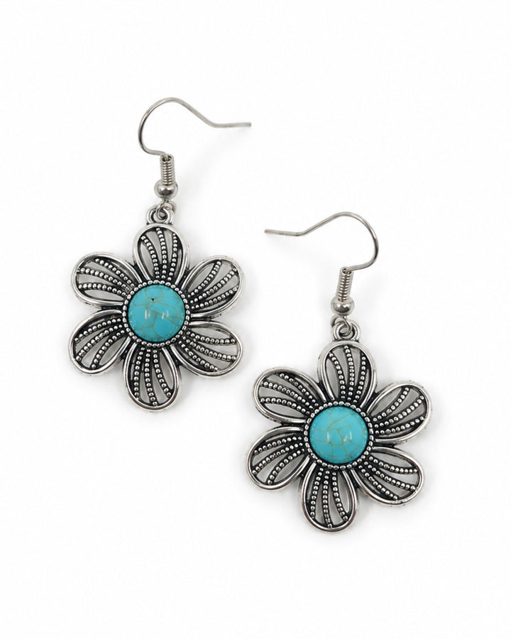 A pair of silver-tone dangle earrings shaped like stylized flowers, featuring a central turquoise blue stone surrounded by textured petal-like filigree details, shown on a plain white background.