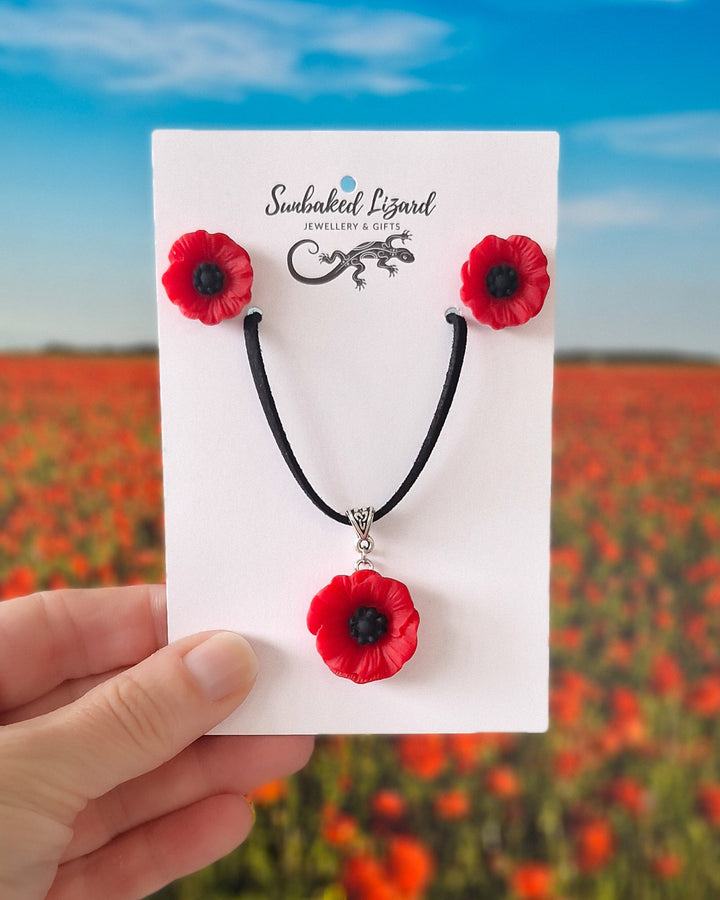 Red poppy necklace and matching stud earrings set on Sunbaked Lizard card with a poppy field background
