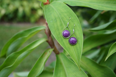 Purple stone earrings on a green leaf with a blurred natural background