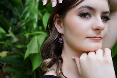Side view of woman wearing purple stone earrings with a green leafy background