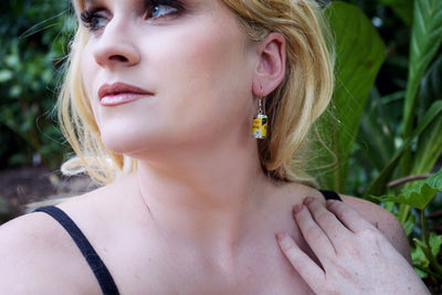 Close up view of woman wearing run tin can drop earrings outdoors with greenery in the background