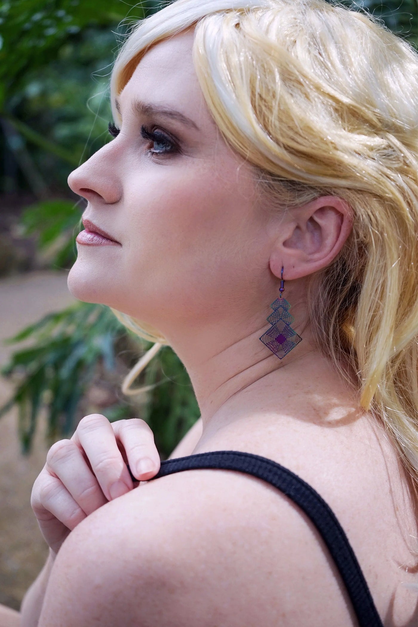 Close-up of a woman wearing iridescent geometric earrings with a blurred green background
