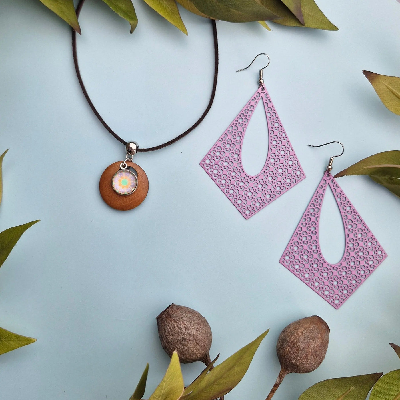 Earrings and necklace displayed surrounded by leaves on a light background.