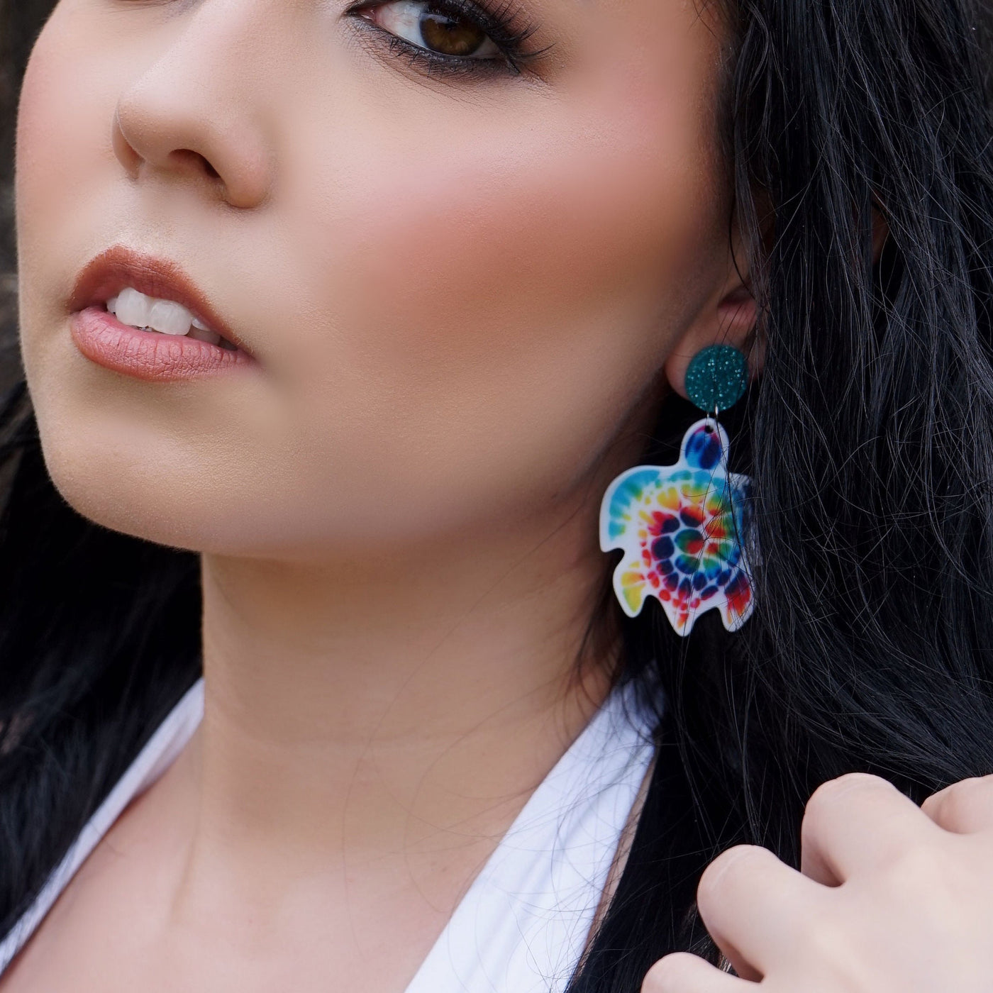 Woman wearing colorful tie-dye turtle earrings with a blurred background