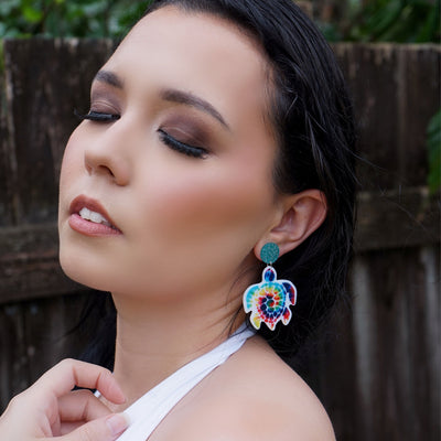 Woman wearing colorful turtle earrings with a blurred natural background
