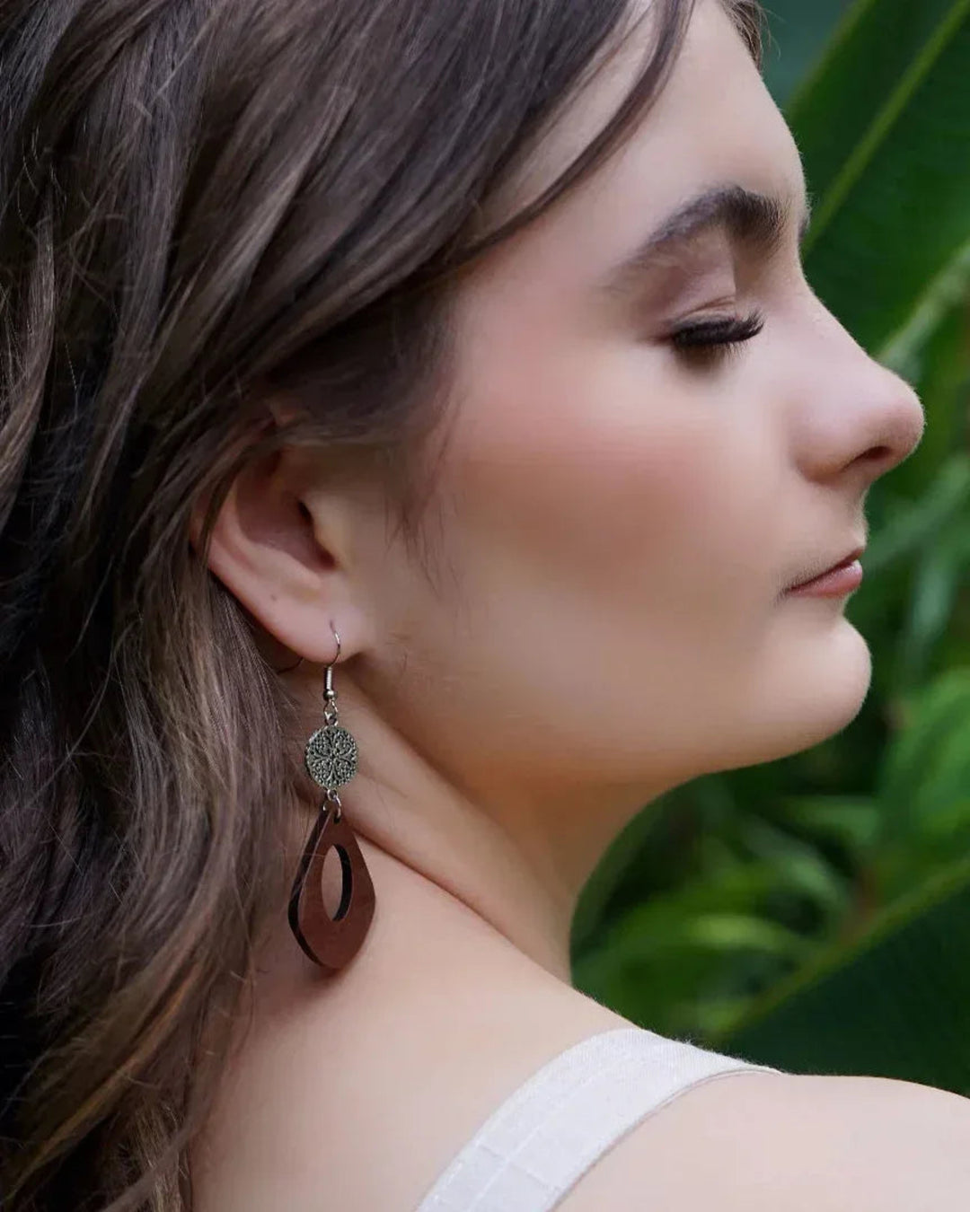 Woman wearing silver and timber dangle earrings with a green leafy background