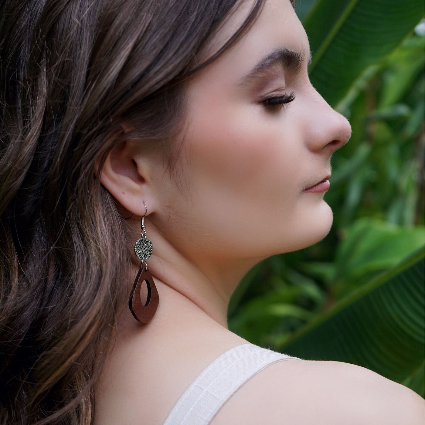Woman wearing silver and timber dangle earrings with a green leafy background