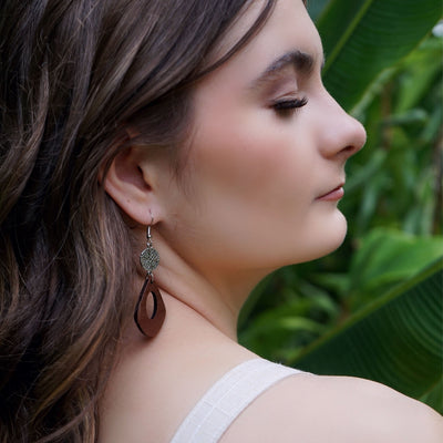 Woman wearing silver and timber dangle earrings with a green leafy background