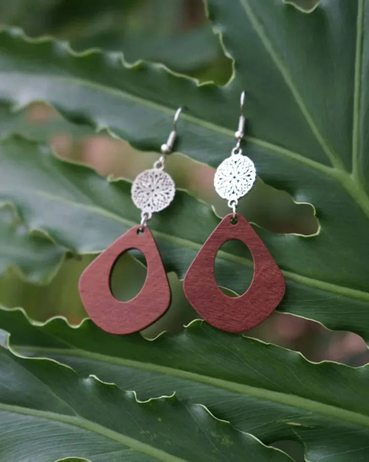 Timber and Silver Floral Pendant Earrings resting on a green large leaf