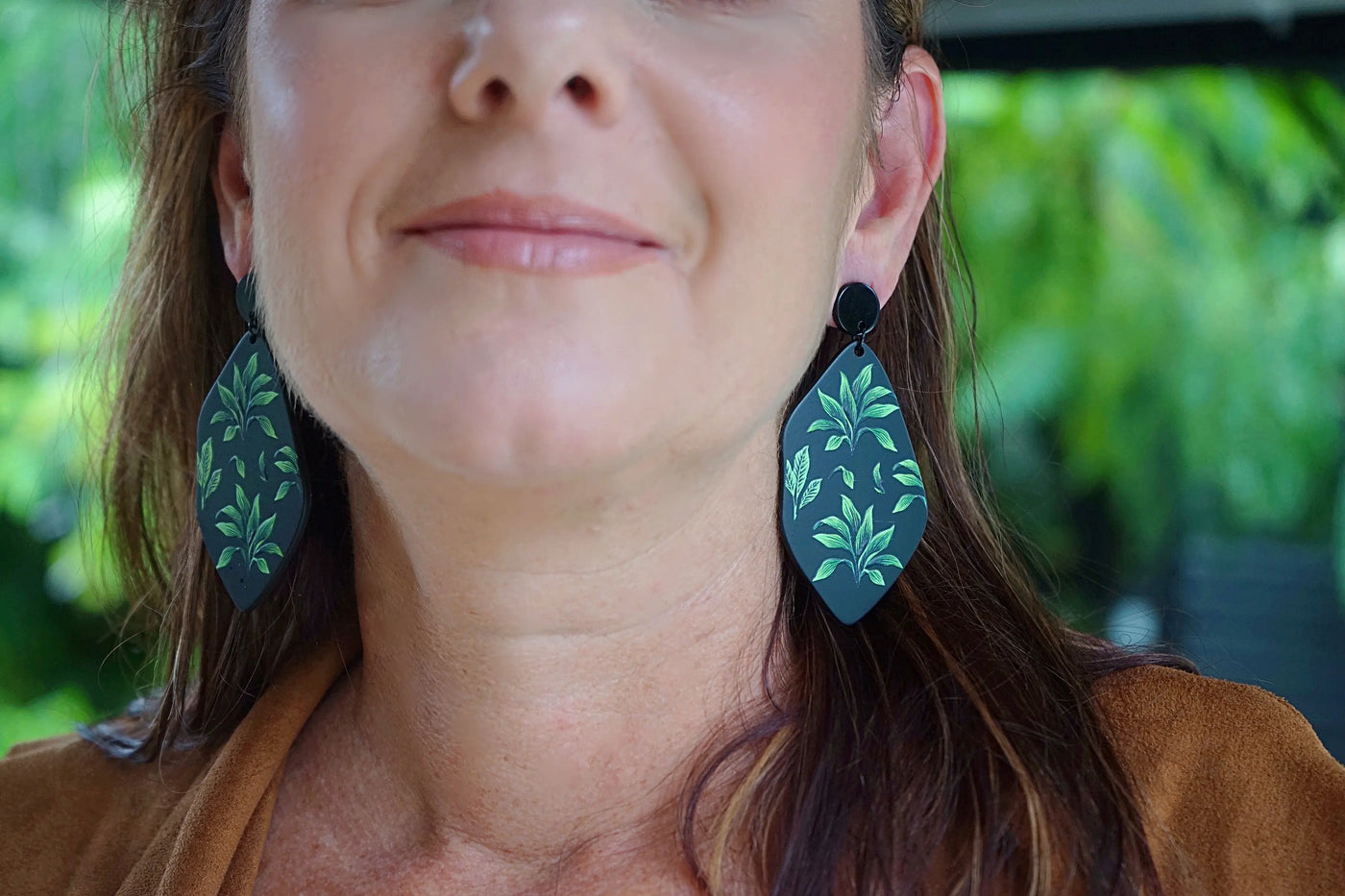 Close up front view of woman wearing tropical fern earrings in natural light