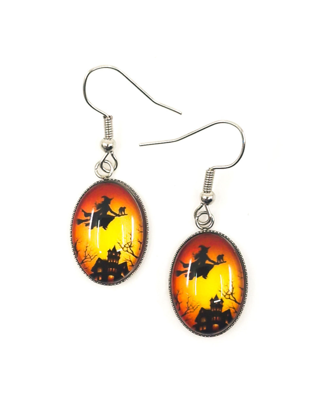 Glass oval Halloween earrings showing witch and cat flying over haunted house at sunset, silver hooks