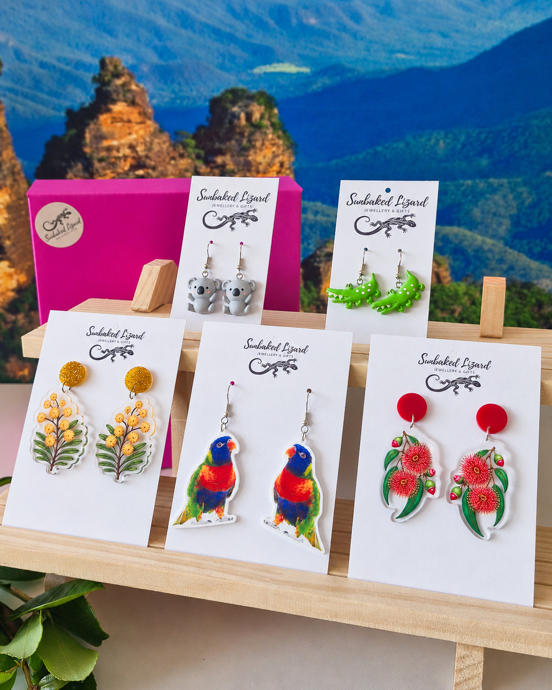 Australian Native Earrings Gift Box, five pairs of Australian earrings on Sunbaked Lizard cards, including wattle, a koala, and a rainbow lorikeet, with the Three Sisters in the Blue Mountains behind