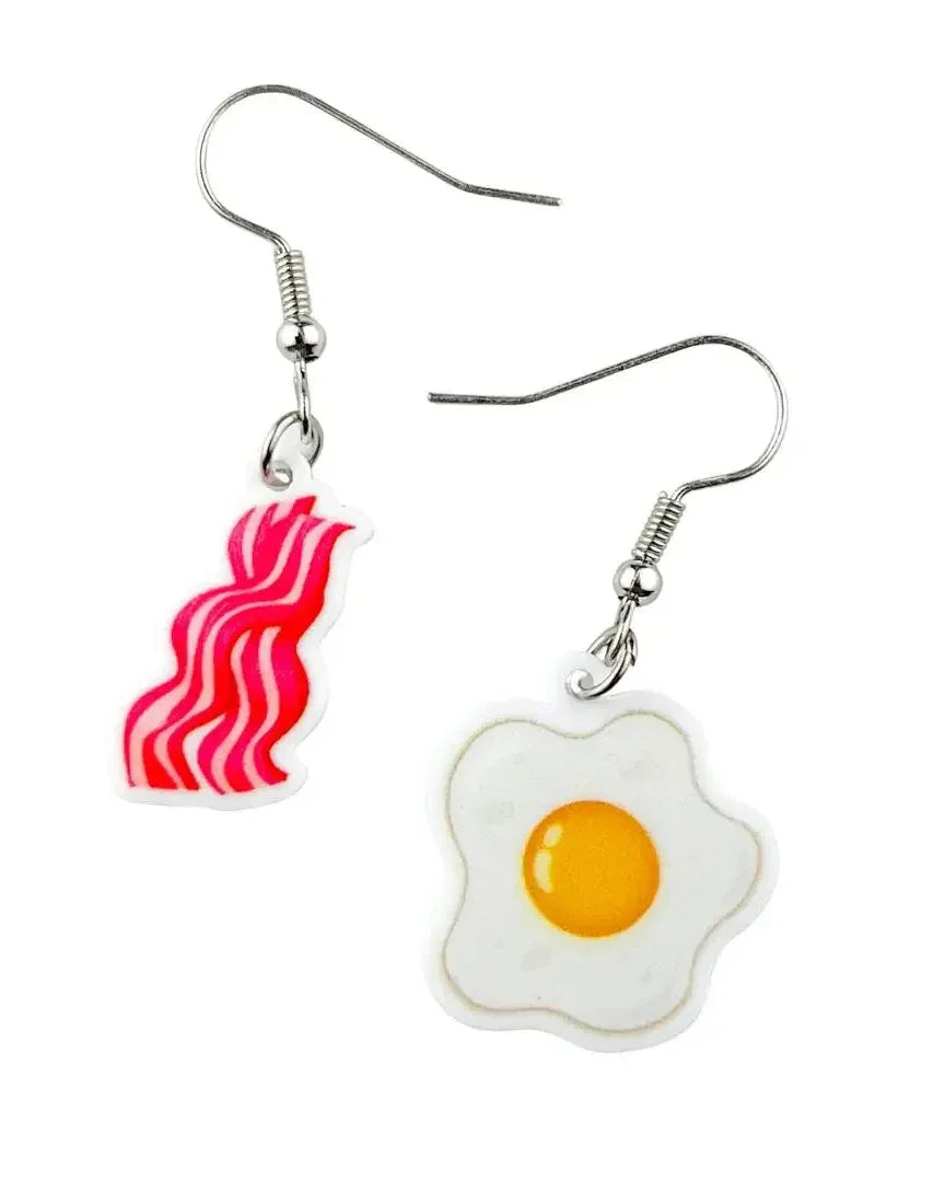 Bacon and egg dangle earrings on silver hooks, a bacon rasher and fried egg charm worn as a mismatched pair