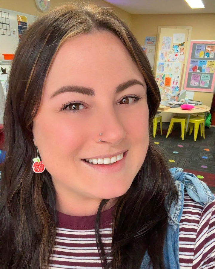 Best Teacher Ever Earrings featuring a red apple design, worn by @two.bright.teachers with a striped top and blue denim pinafore.