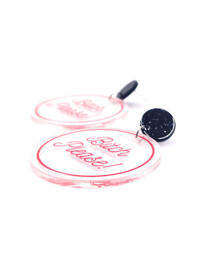 Close-up of Bitch Please acrylic statement earrings with pink script, clear round charms and glitter black studs.