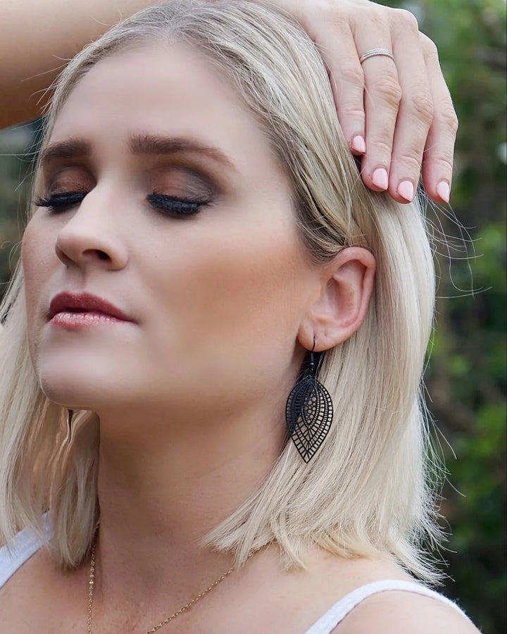 Model wearing black botanical leaf dangle earrings showing length and filigree-style cut-out detail