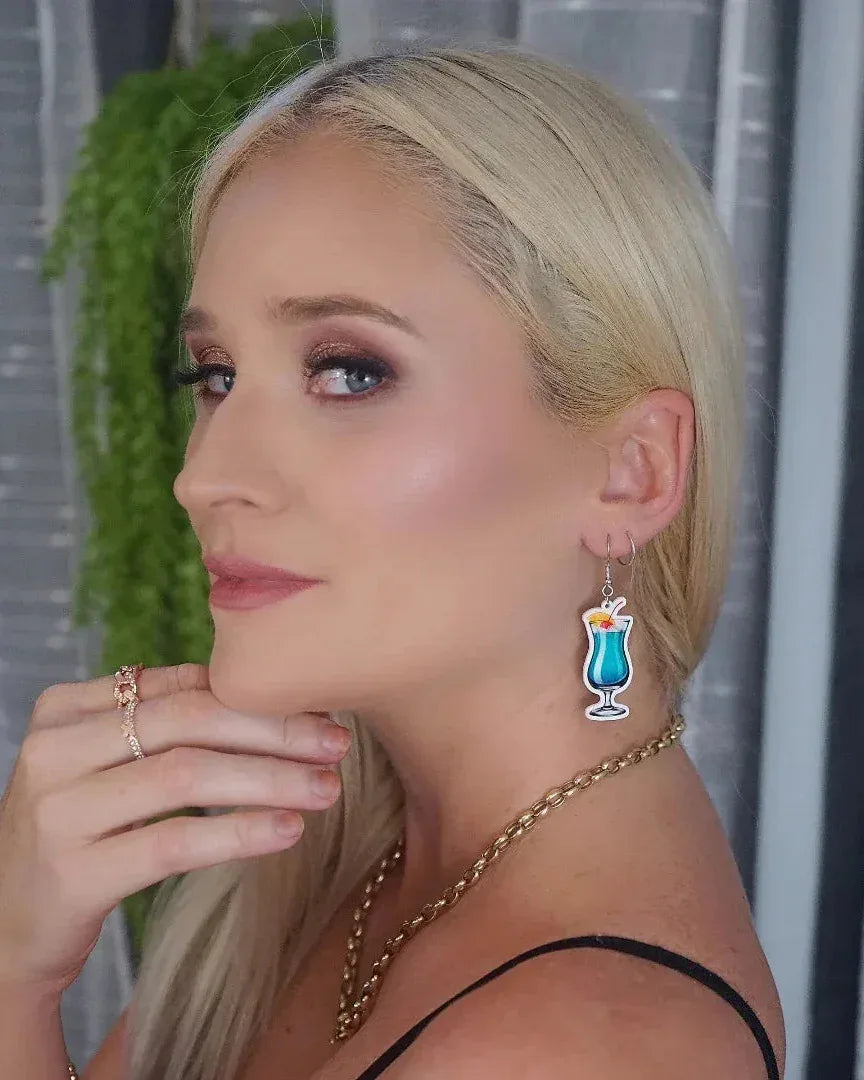 Woman wearing blue cocktail drink drop earrings with cherry and orange garnish