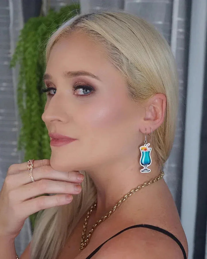 Woman wearing blue cocktail drink drop earrings with cherry and orange garnish