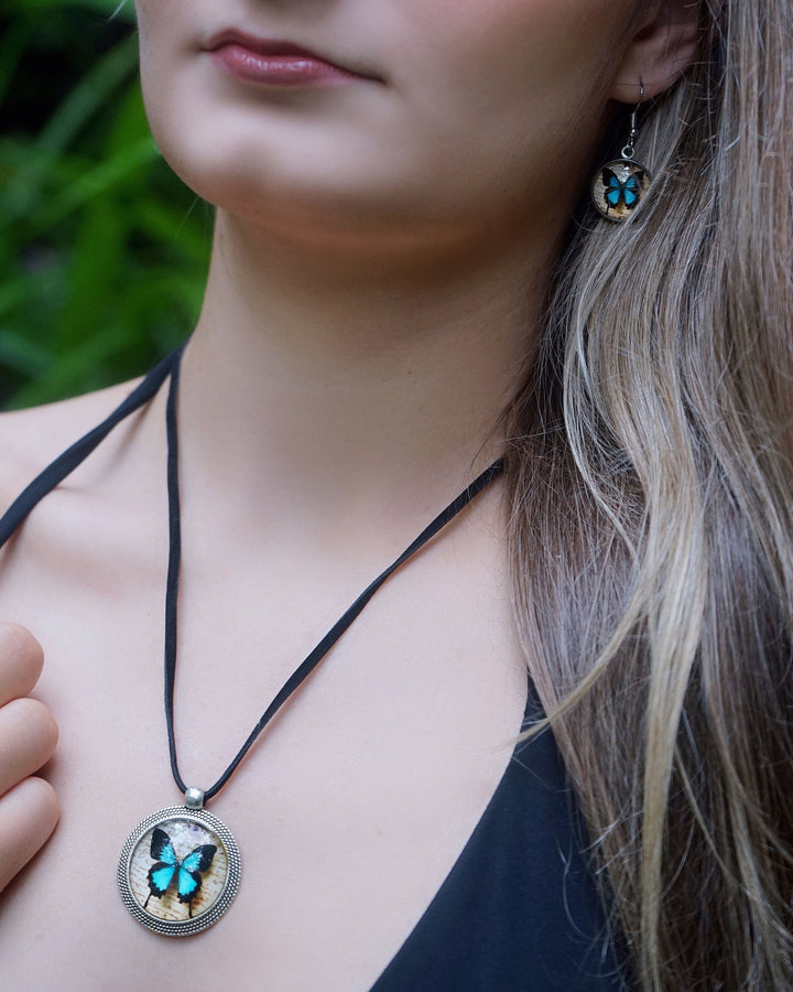 Close-up of blue Ulysses butterfly necklace on black cord with matching butterfly earring worn by model