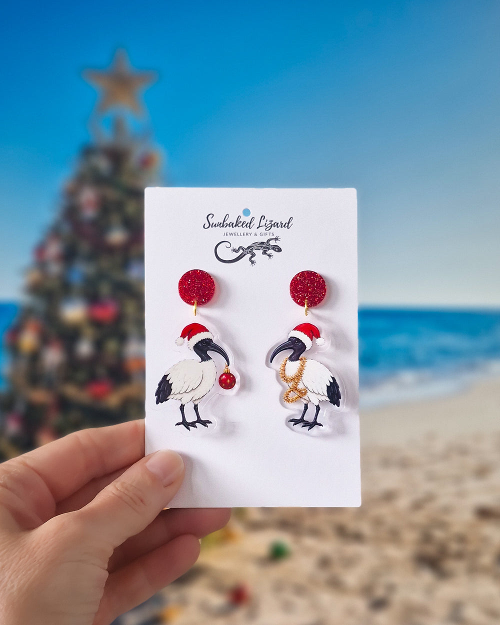 Christmas bin chicken earrings with red glitter tops, Santa hats and festive ornaments on a beach Christmas background.