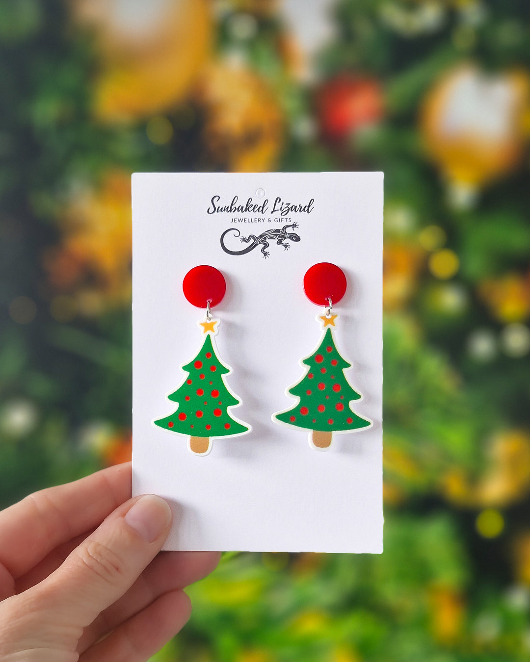 Christmas tree earrings with red disc tops, bright green tree charms, red baubles and gold stars on a festive green background.