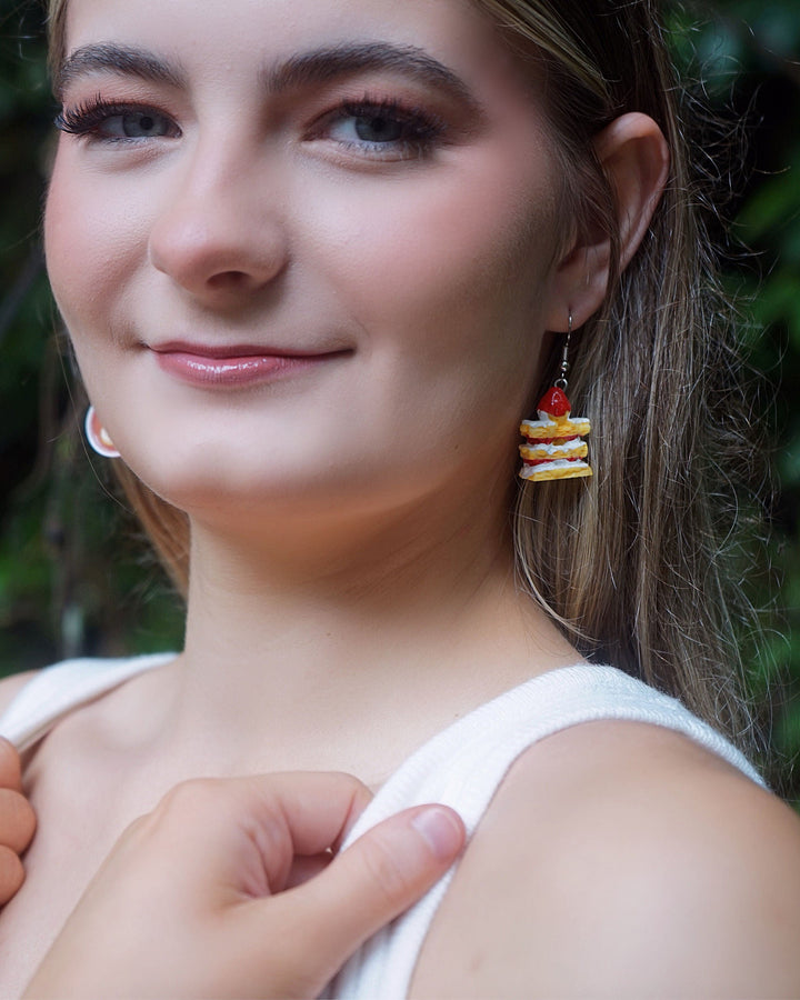 Model wearing Coffee and Cake earrings, with a close-up of the strawberry cake earring from the mismatched food earring set.