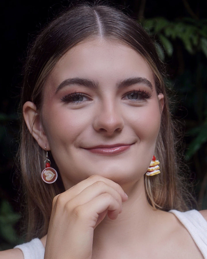 Model wearing mismatched Coffee and Cake Earrings featuring one latte earring and one strawberry cake earring.