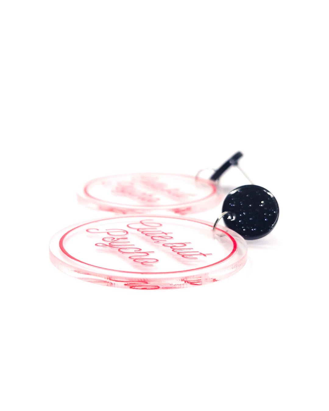 Close-up of Cute But Psycho acrylic statement earrings with pink script, clear round charms and glitter black studs.