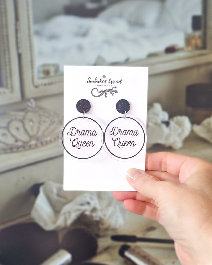 Drama Queen black acrylic statement earrings displayed on a Sunbaked Lizard card at a vanity table.
