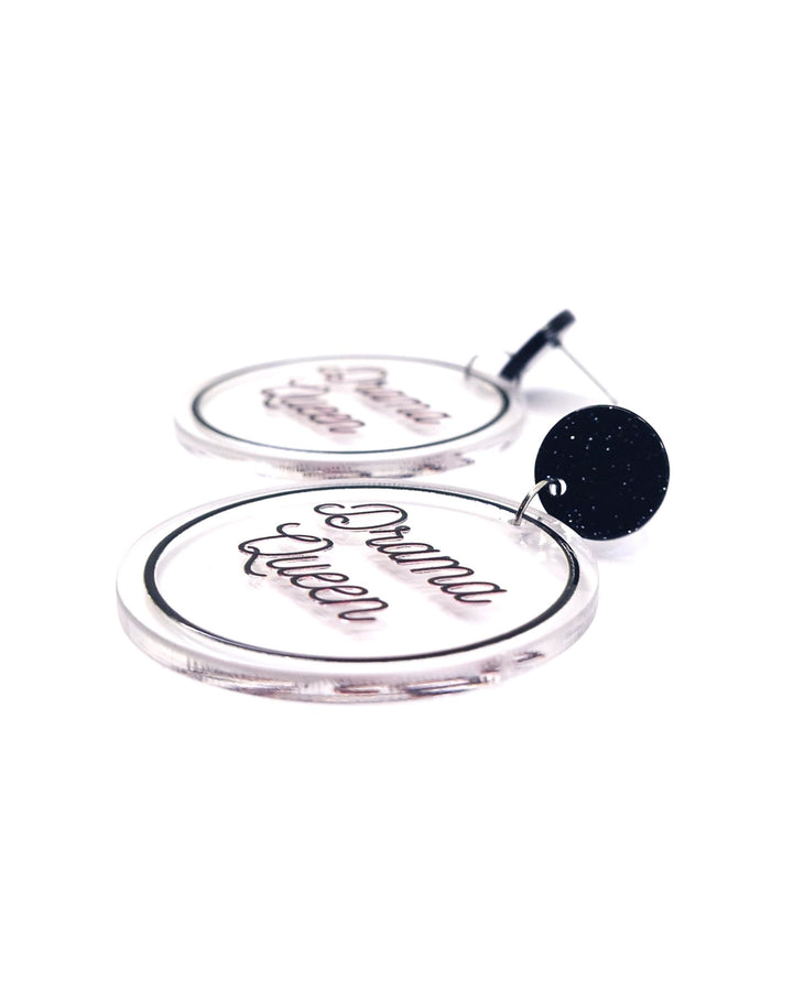 Close-up of Drama Queen acrylic statement earrings with black script, clear round charms and glitter black studs