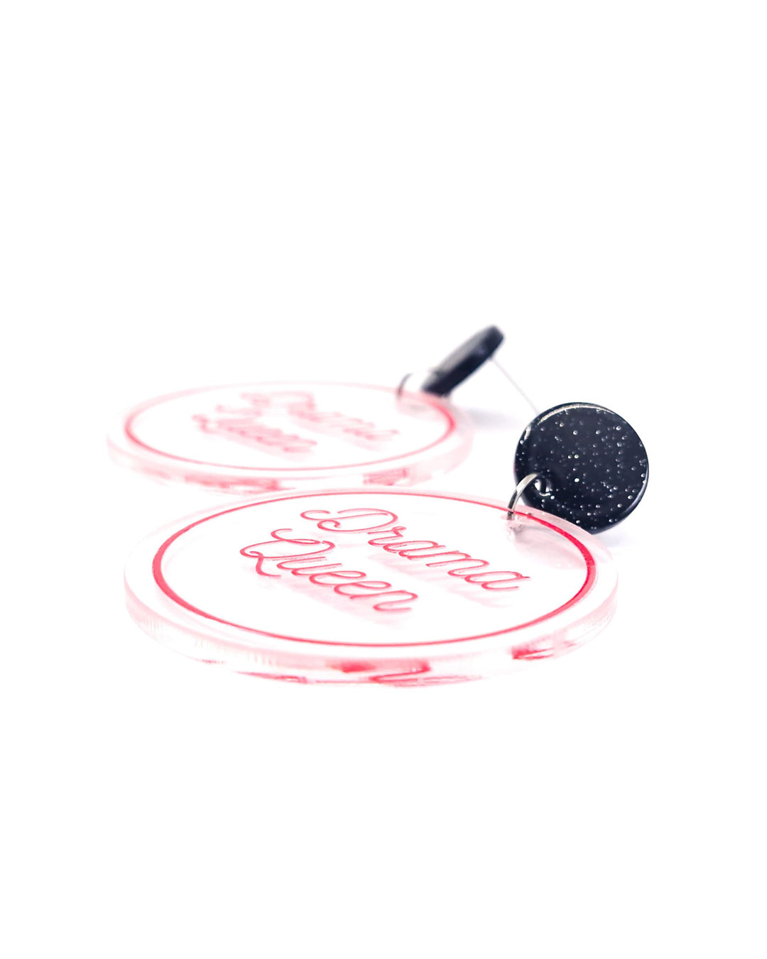 Close-up of Drama Queen acrylic statement earrings with pink script, clear round charms and glitter black studs