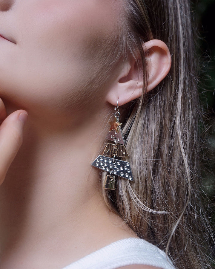Close-up of a model wearing Elegant Christmas Tree Earrings featuring layered metallic tree charms with silver and gold accents.