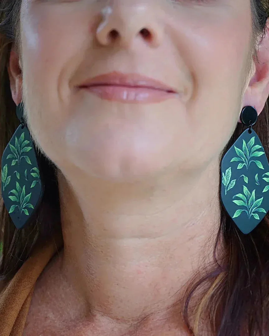 Model wearing fern tropical plant drop earrings in matte black and green