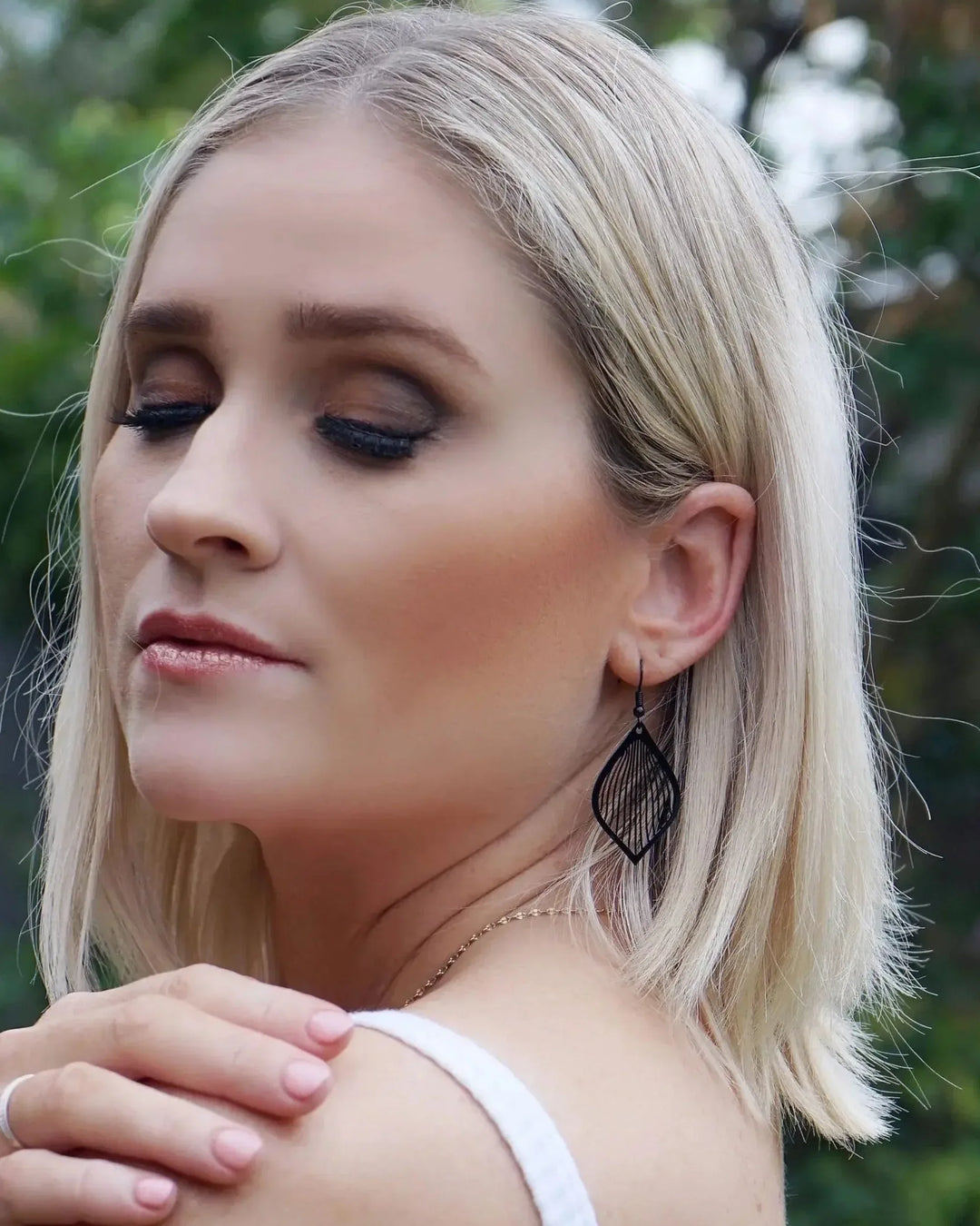 Model wearing black filigree teardrop drop earrings with fine lined cut-out detail