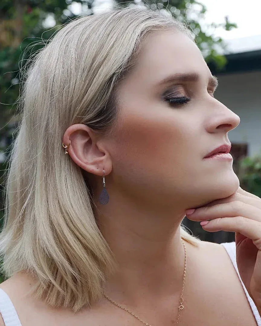 Side profile of model wearing deep blue filigree teardrop drop earring with delicate cut-out detail