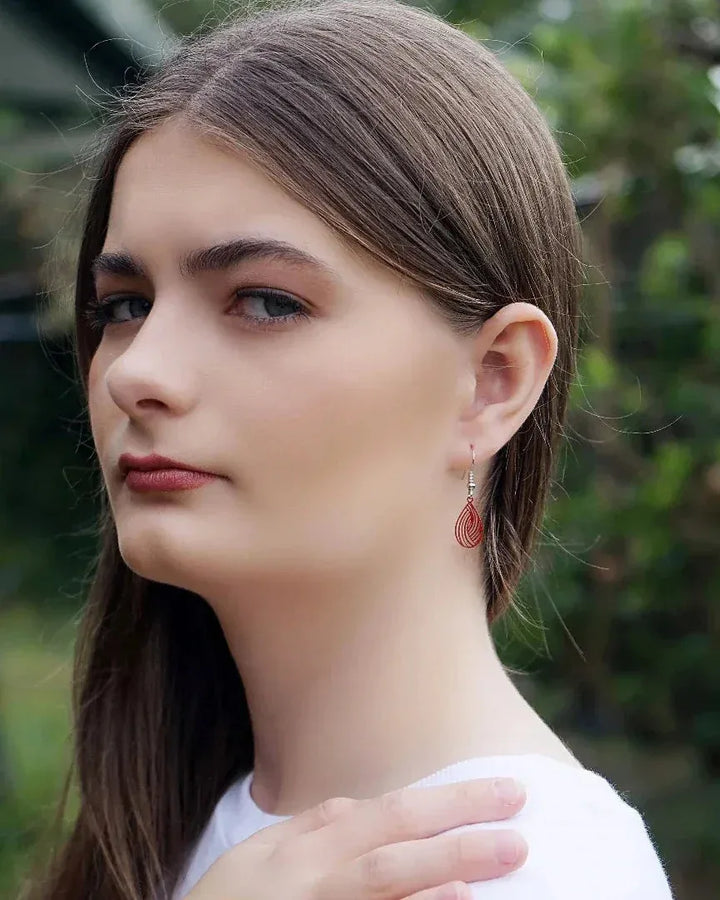 Model wearing red filigree teardrop drop earrings with petite drop length and fine cut-out swirl pattern