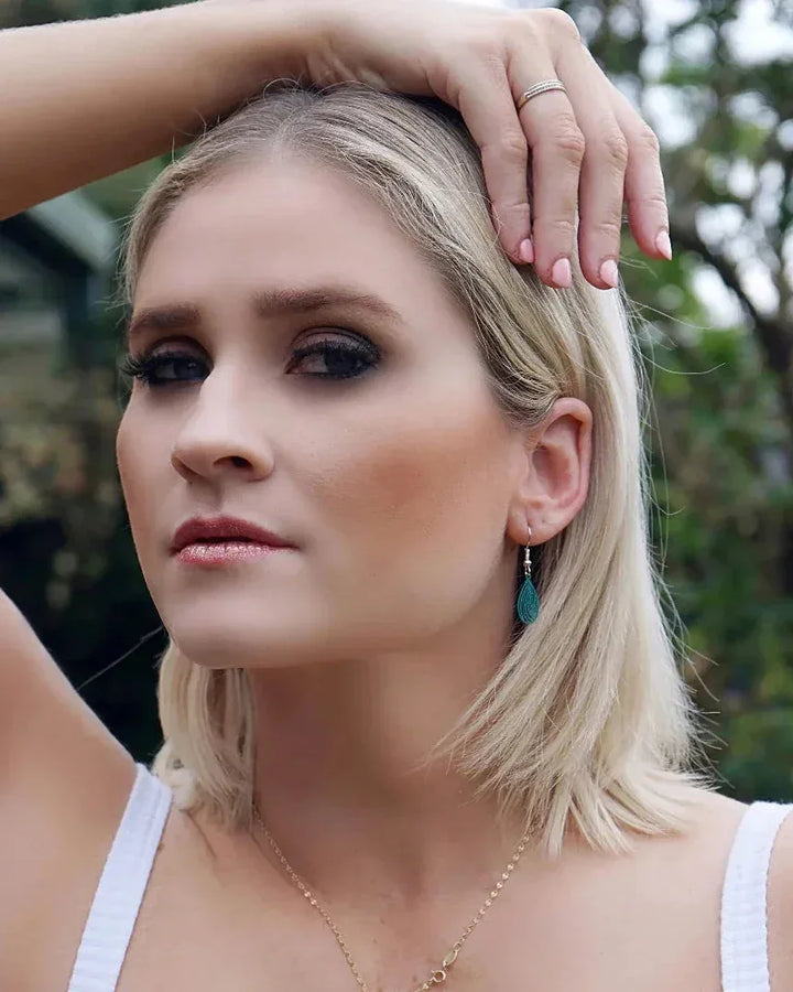 Model wearing teal filigree teardrop drop earrings showing petite size and delicate cut-out detail