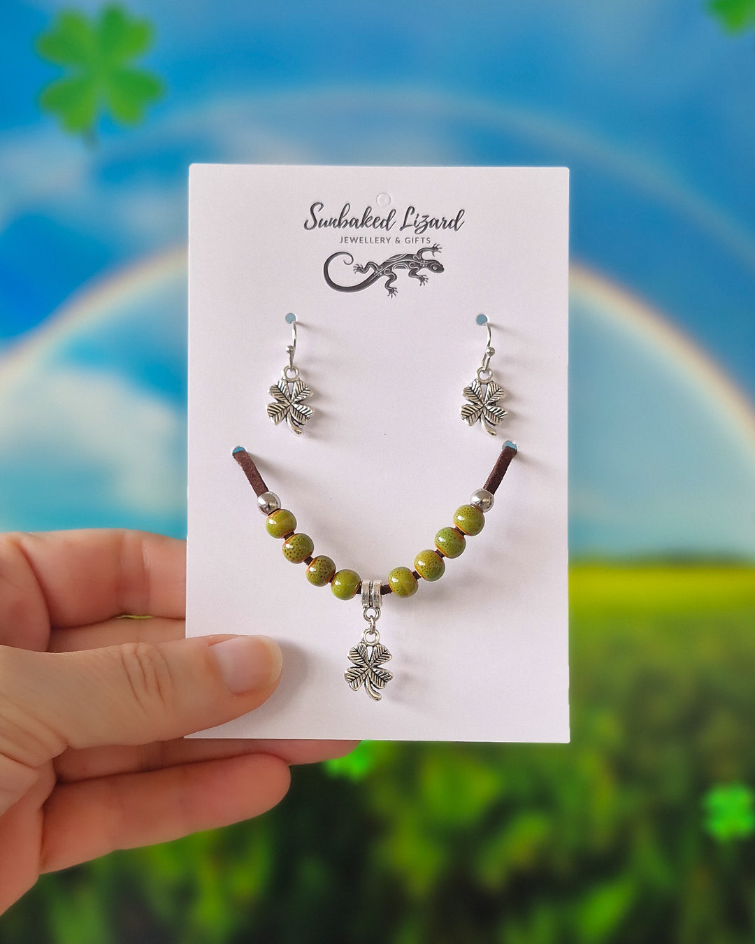 Four leaf clover matching set, silver-tone clover earrings and a green beaded bracelet with a clover charm on a Sunbaked Lizard card