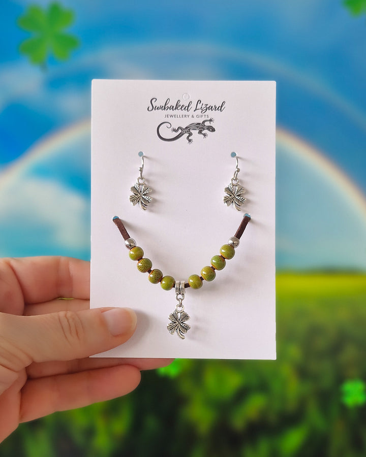 Four leaf clover matching set, silver-tone clover earrings and a green beaded bracelet with a clover charm on a Sunbaked Lizard card